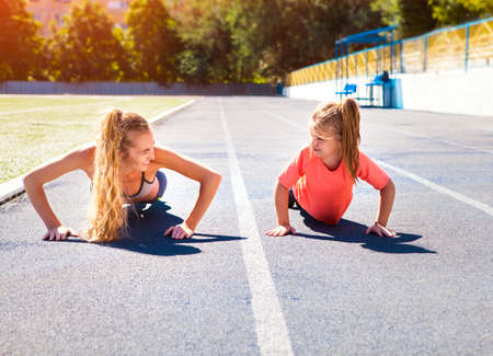 Mother and little daughter are doing exercise in the stadium. Family doing fitness at the stadium. Healthy family conceptの写真素材