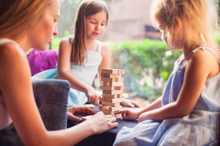 Happy mother with two children playing the wooden blocks tower at home