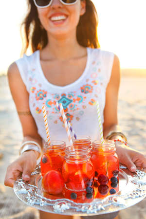 Happy young woman holding a dish with a drinks at summer beach partyの写真素材