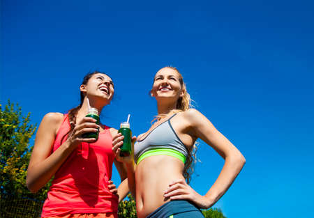 Two happy women drinking vegetable smoothie after fitness running workout on stadium. Fitness and healthy lifestyle conceptの写真素材