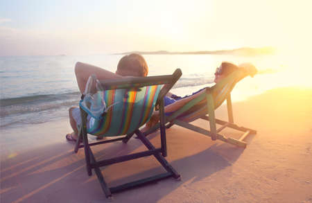 Happy couple sitting at sun chairs on the beach of Koh Samet at sunset, Thailandの写真素材