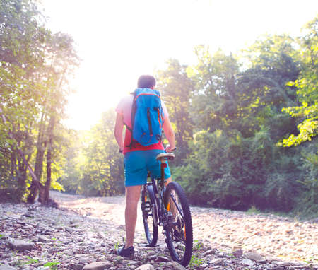 Young athlete man crossing mountain river with bicycleの写真素材