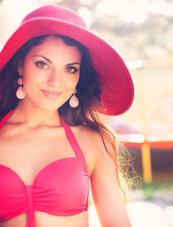 Young brunette fashionable woman in red hat posing in a red bikiniの写真素材