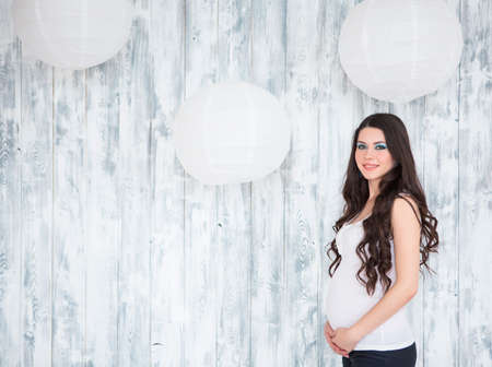 Portrait of beautiful smiling pregnant woman wearing casual jeans over wooden white backgroundの写真素材
