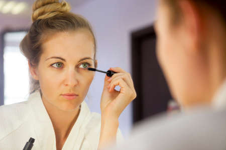 Young blond woman applying make up looking at mirrorの写真素材