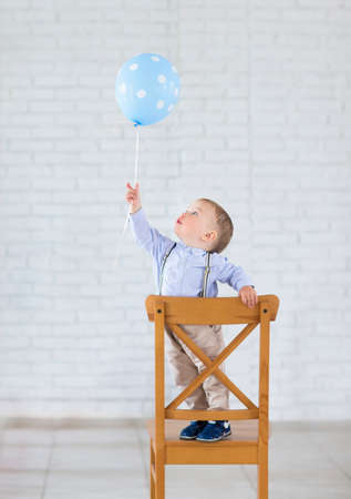 Cute little baby boy with one balloon standing on the chairの写真素材