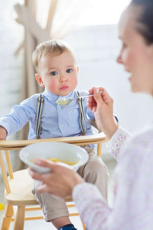 Beautiful young woman feeds her baby son at home