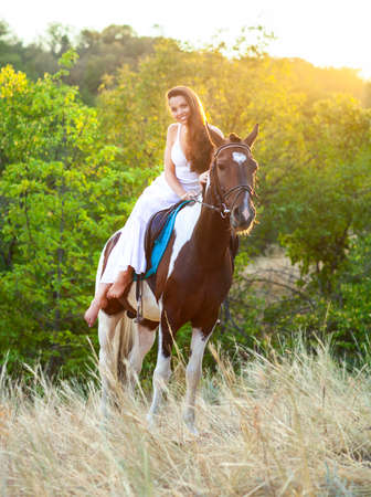 Young woman riding a horse at sunsetの写真素材