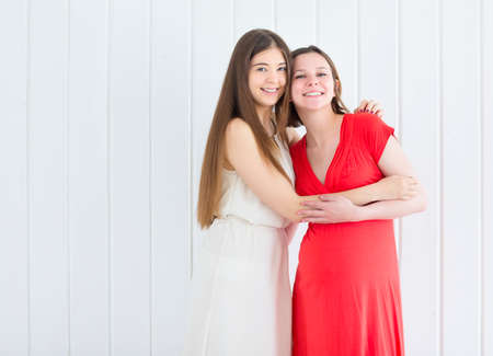 Female friend with pregnant woman on white backgroundの写真素材