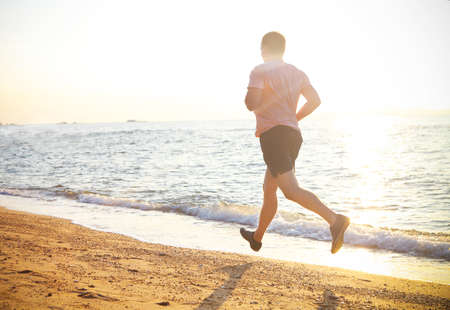 Young man running on the beach at sunsetの写真素材