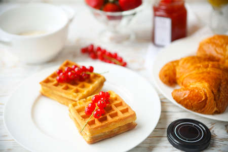 Waffles with red currant jam and berries on a white plate, croissants, orange juice and oat flakes oatmeal on the wooden backgroundの写真素材