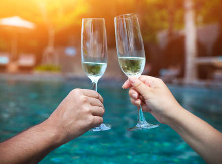 Couple holding glasses of champagne making a toast by the poolの写真素材