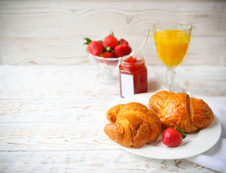Two tasty croissants on the plate and strawberry jam on wooden backgroundの写真素材