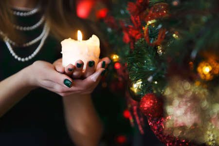 Attractive brunette young woman holding a burning candle celebrating Christmas. Close up