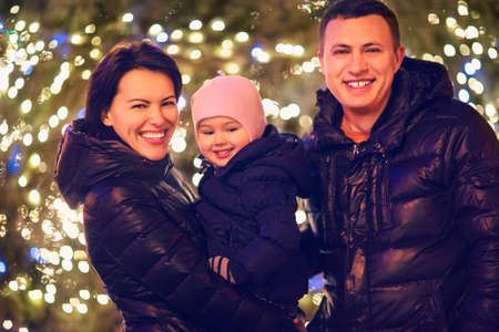 Happy family with little daughter looking at camera outside over Christmas backgroundの写真素材