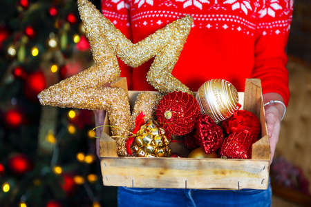 A woman holds a box with a lot of Christmas decorations near X-mas tree. Xmas holiday concept.の写真素材