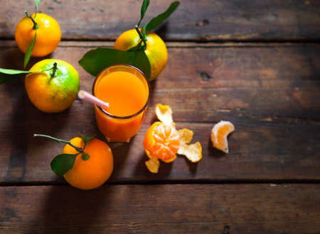 Glass of fresh tangerine juice with ripe tangerines, leaves and old-fashioned strawの写真素材