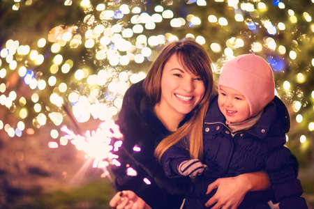 Mother and little daughter with Bengal light outside over Christmas backgroundの写真素材
