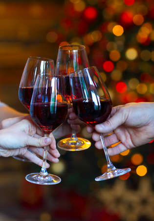 Clinking glasses of wine in hands on bright christmass tree lights background. Event celebrationの写真素材