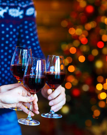 Clinking glasses of red wine in hands on Christmas lights background. X-mas party conceptの写真素材