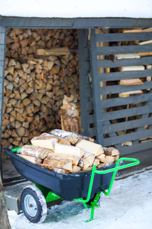 Firewood stacked in winter. Wood pile with snow stacked for firewood. Cart with wood.の写真素材
