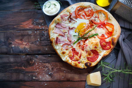 Pizza carbonara with bacon, salami, parmesan cheese and chicken egg on the wooden rustic tableの写真素材