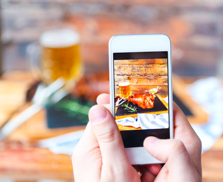 Wiman making photo on phone of roasted pork leg (rulka) served with garlic sauce on the wooden table