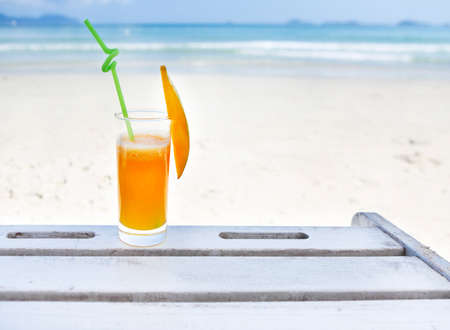 Glass of orange colour juice on the beach. Mango juice and slice on white tableの写真素材