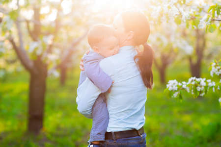 Little baby boy with his young mother in the blossoming spring gardenの写真素材