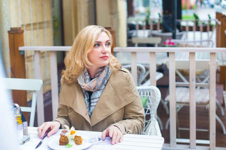 Close up happy middle age blond woman in outdoors cafe looking into distance.の写真素材