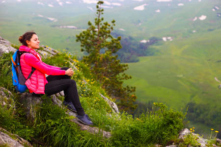 Hiker with backpack relaxing on top of a mountain and enjoying valley view during sunriseの写真素材