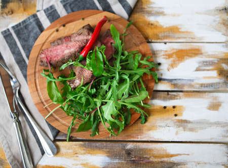 Sliced medium rare grilled Beef steak Ribeye with rocket salad on cutting board on wooden background の写真素材