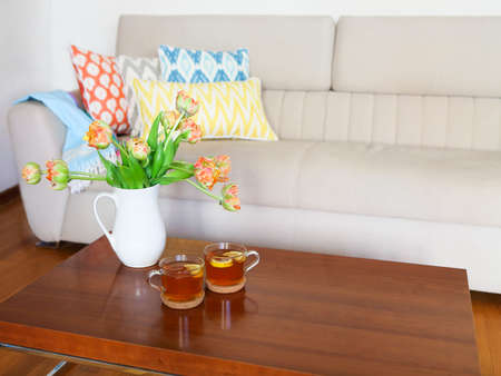 Beautiful orange tulips bouquet with two cups of tea on wooden table in the living room