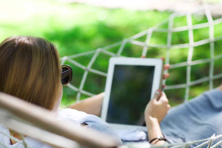 Lazy time. Woman in hat in a hammock with tablet computer on a summer day の写真素材