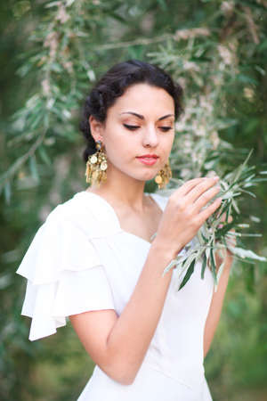 Portrait young bride with brunette hair in white wedding dress and vintage gold jewelry earrings over blurred outdoors backgroundの写真素材