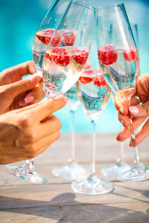 People hold Champagne glasses with raspberry. Summer pool partyの写真素材