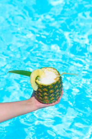 Hand with Pineapple exotic coctail near swimming pool Pina colada