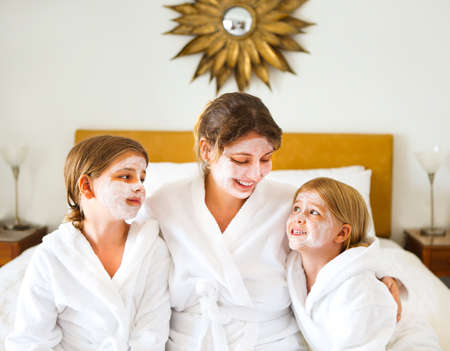 Happy mother and girls in bathrobes with cream mask. Family care and spa conceptの写真素材