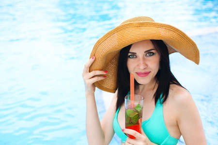 Real female beauty enjoying her summer vacation at swimming pool with alcohol cocktailの写真素材