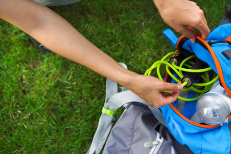 Sporty woman sitting on the green grass with jump rope, backpack and drink bottle. Close up
