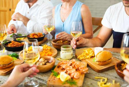 Hands with white wine toasting over served table with food. Friendship and happiness conceptの写真素材