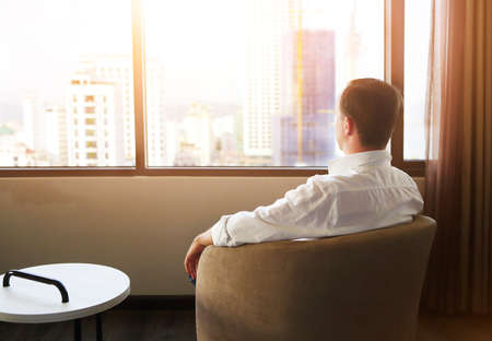 Rear view of man relaxing on chair in the hotel roomの写真素材