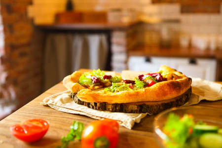 Homemade pizza and vegetables on wooden table in the kitchenの写真素材