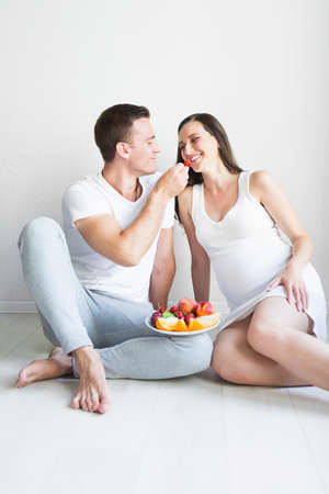 Young man and pregnant woman with fruit plate in the kithen. Pregnancy and nutrition concept