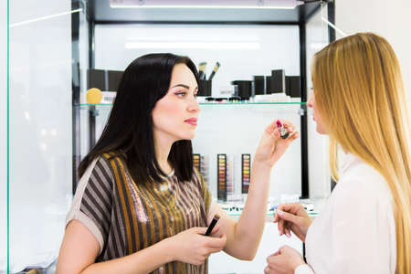 Young pretty woman chosing color cosmetic and beauty consultant in shop or beauty salonの写真素材