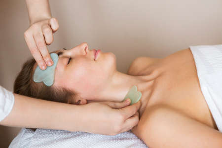 Young woman have face guasha treatment at asian beauty clinicの写真素材