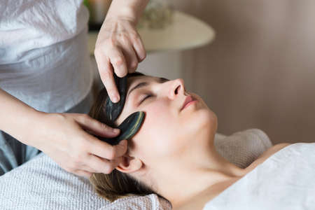 Young woman have face guasha treatment at asian beauty clinic