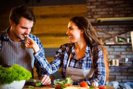 Young man and woman cooking and eating together at kitchenの写真素材