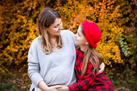 Happy young pregnant mother hugging with teen daughter in autumn park. Happy family conceptの写真素材