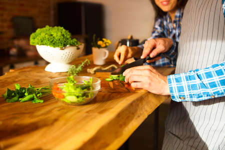 Young man and woman cooking vegetable salad together at kitchenの写真素材